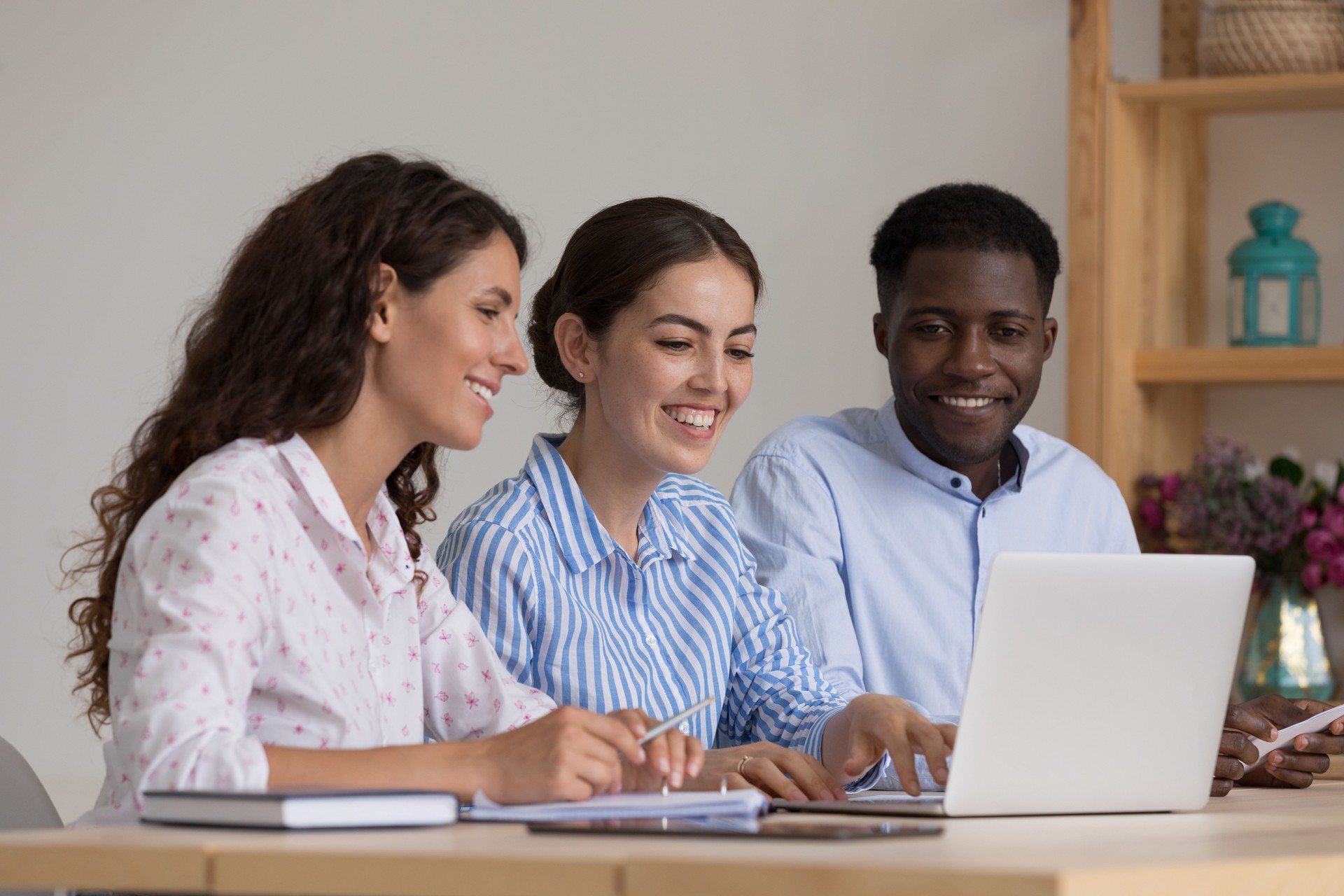 Diverse group of happy interns and mentor talking at laptop