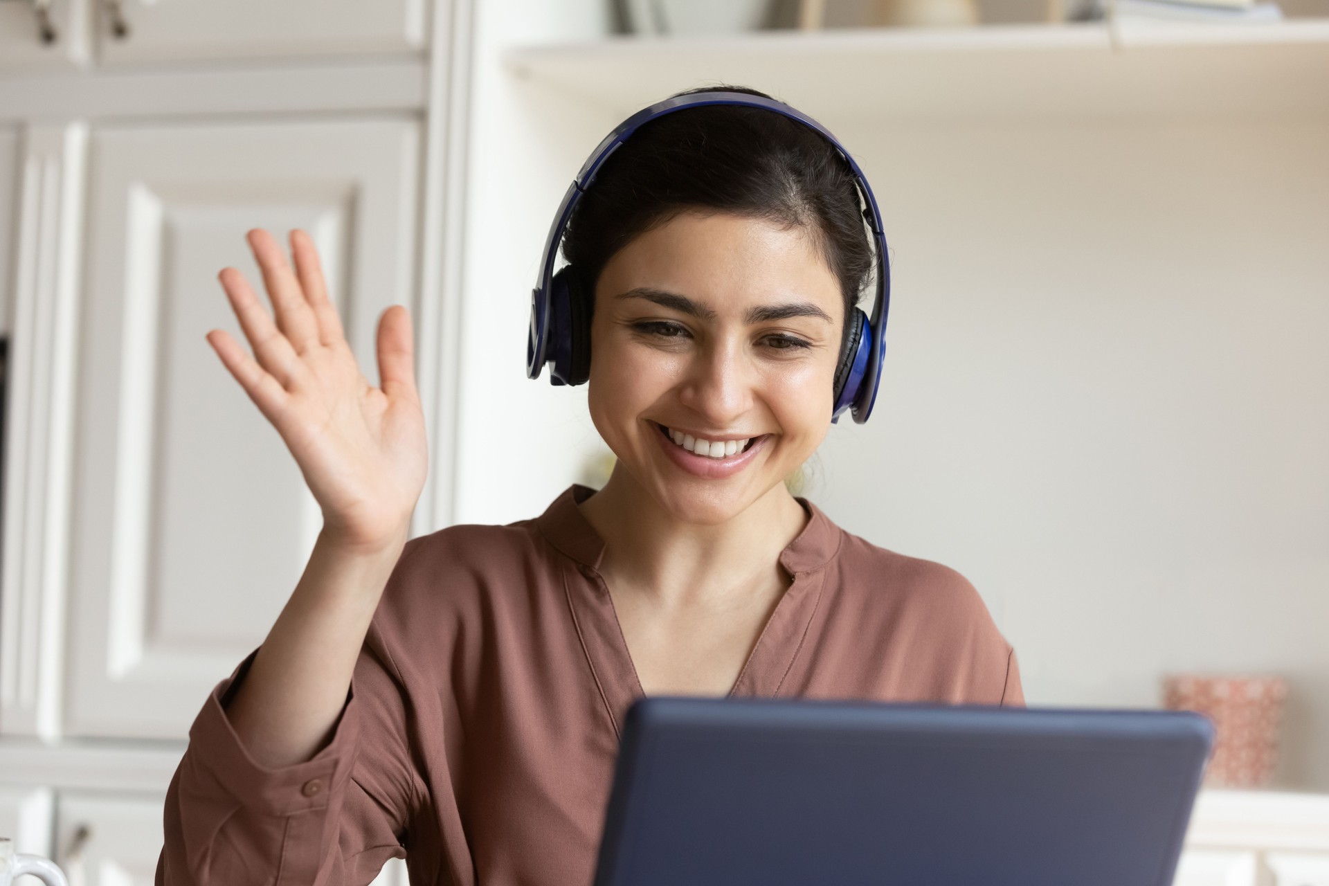 Friendly indian female in earphones wave hand before pad webcam